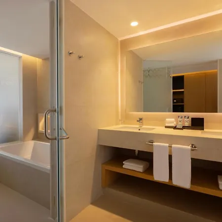 Royalton Splash Riviera Cancun, An Autograph Collection All-Inclusive Resort Puerto Morelos Facilities photo The photo shows a modern and well-lit bathroom. The main focus is a double vanity with a light-colored countertop and two sleek, modern faucets. Below the countertop, there's a wooden shelf holding neatly folded white towels. 

Behind the vanity is a