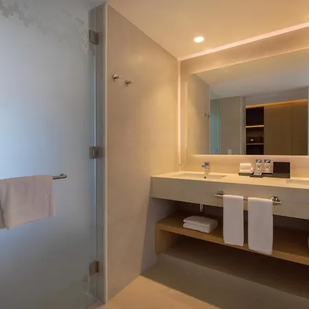 Royalton Splash Riviera Cancun, An Autograph Collection All-Inclusive Resort Puerto Morelos Facilities photo The photo shows a modern and bright bathroom. The walls are a light beige color, and the floor is a light-colored tile. The bathroom features a glass-enclosed shower with a chrome showerhead and a towel bar holding a folded white towel. 

In the cent